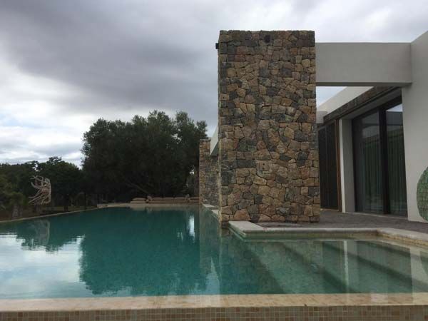 Piscina con pilar de piedra junto a un edificio moderno bajo un cielo nublado.