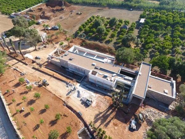 Vista aérea de un edificio moderno en construcción en un campo con árboles y tierra circundantes.
