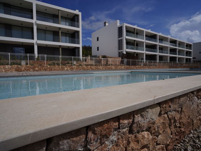 Edificios con balcones con vistas a una piscina, frente a un cielo azul.