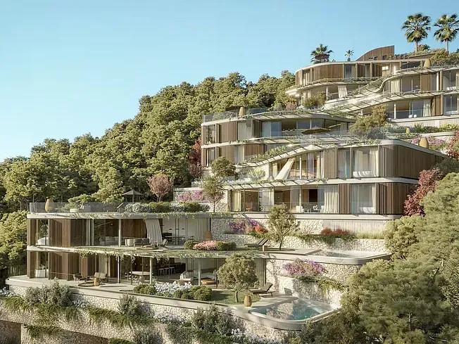 Sitio de construcción con edificios, grúa en una ladera con árboles verdes y casas circundantes.