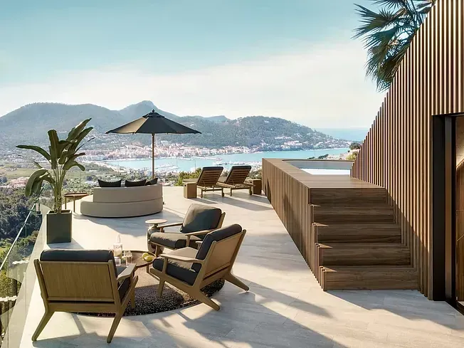 Patio exterior con muebles de salón, pequeña piscina, vistas a un pueblo costero y a las montañas.