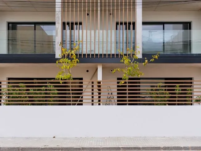 Edificio de apartamentos moderno con fachada de color claro, detalles de madera y cercas horizontales.