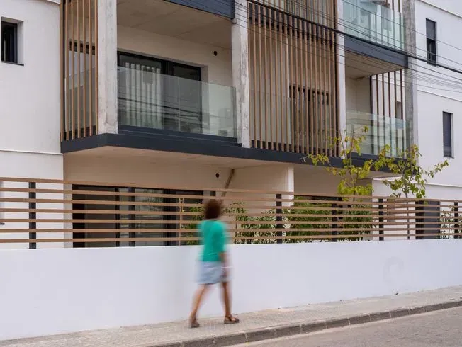 Mujer caminando por una acera frente a un edificio moderno con características de listones de madera.
