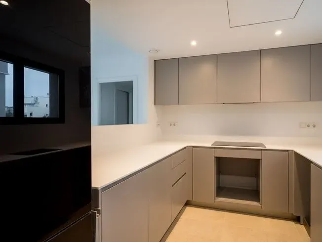 Cocina moderna con gabinetes gris claro, encimeras blancas y refrigerador negro.