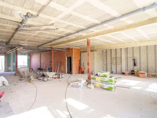 Interior de un edificio en construcción. Paredes sin terminar, tuberías expuestas y materiales de construcción dispersos.