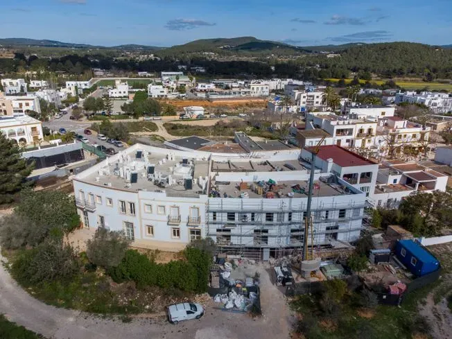 Vista aérea de un edificio circular blanco en construcción en un pueblo con colinas verdes.