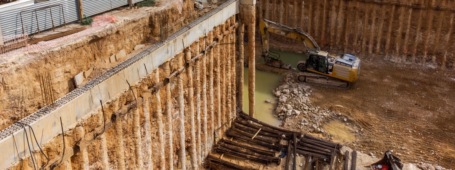Sitio de construcción con una excavadora cavando en un pozo profundo, paredes de tierra marrón.