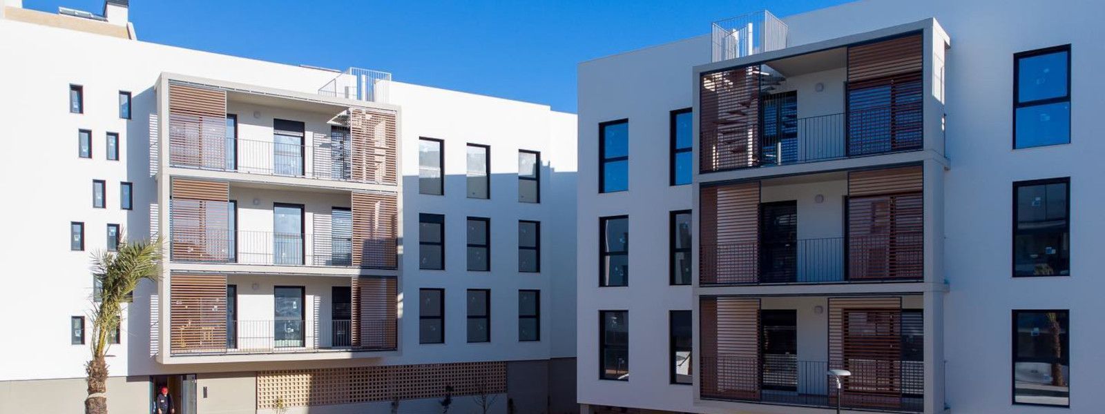 Modernos edificios de apartamentos blancos con detalles de madera y balcones contra un cielo azul claro.