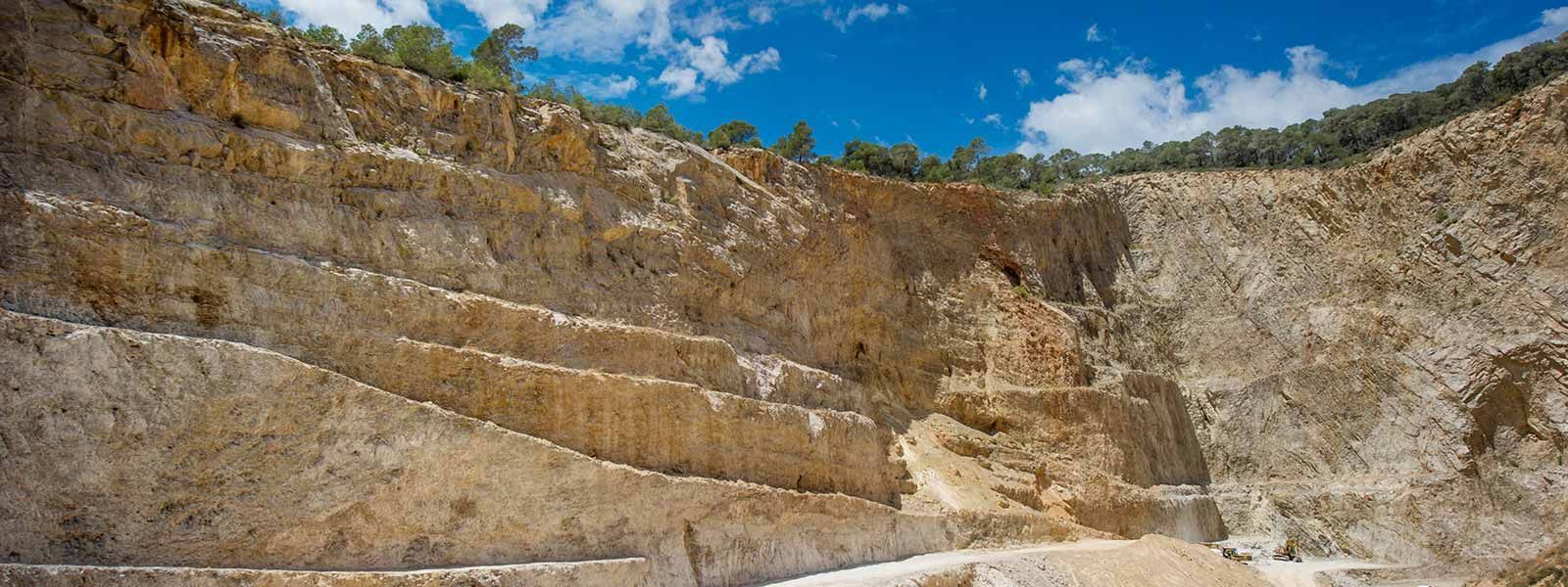 Una cantera con formaciones rocosas estratificadas bajo un cielo azul con algunas nubes.