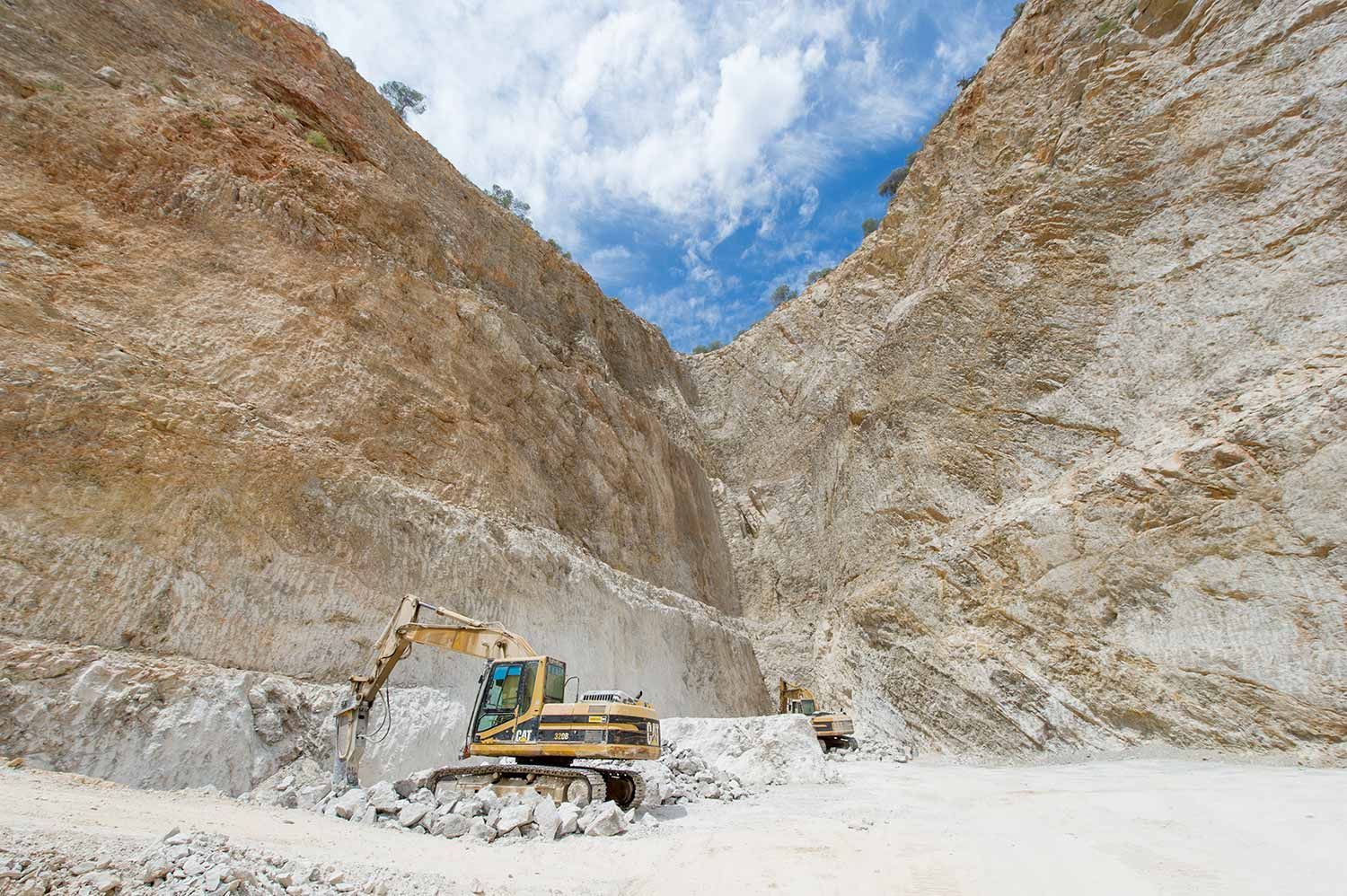 Excavadora en una cantera, extrayendo roca blanca. Cielo azul con nubes.
