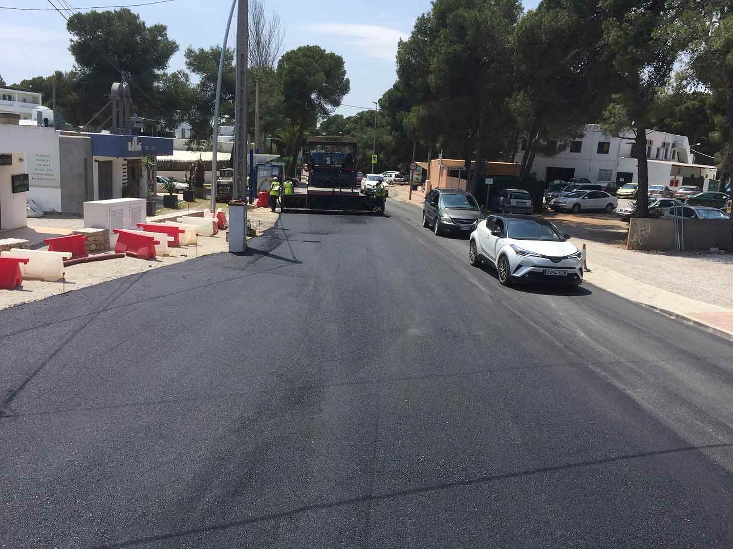 Repavimentación de la carretera en progreso; pavimentación de asfalto, barricadas naranjas, automóviles y trabajadores visibles.