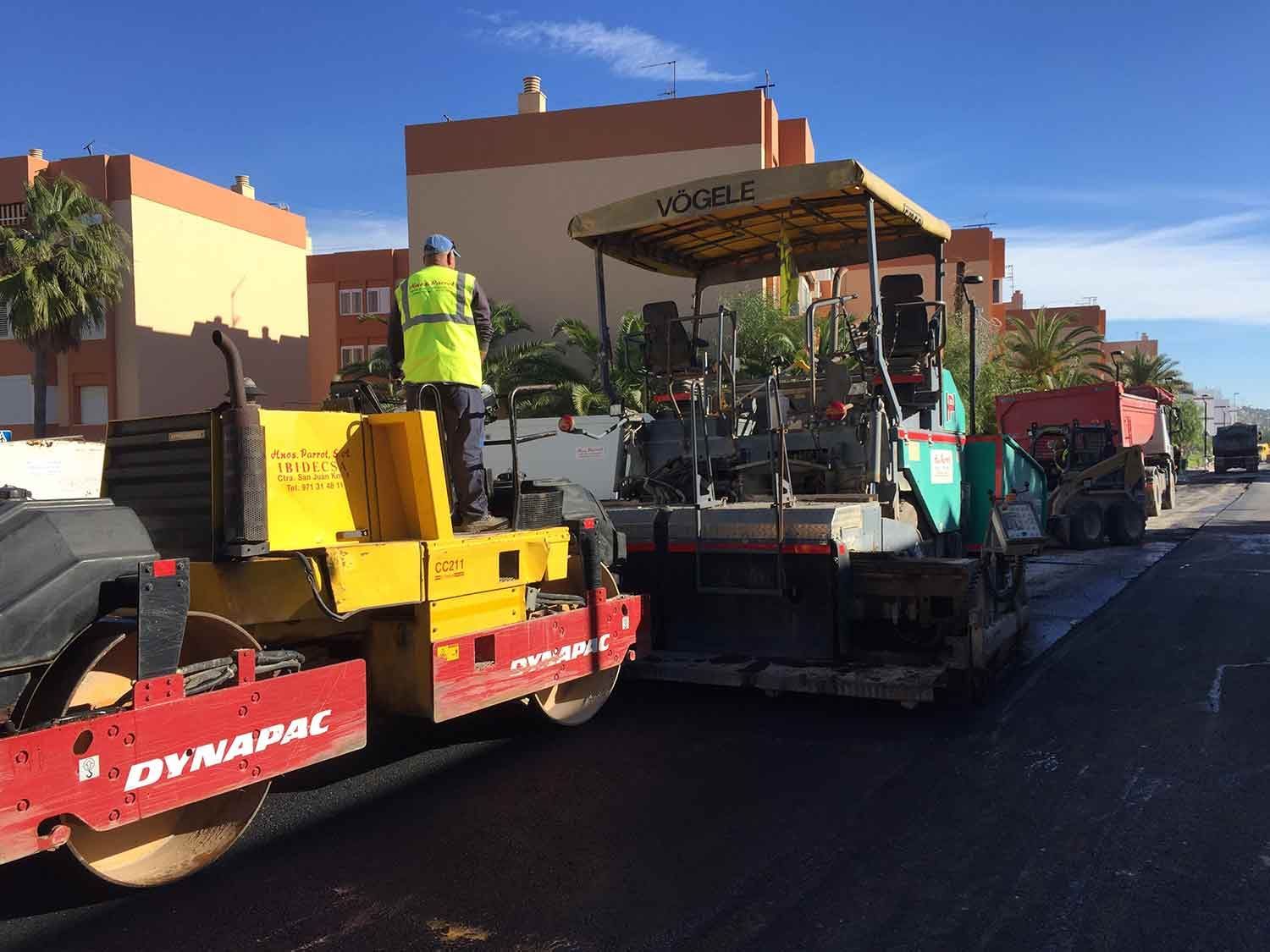 Pavimentación de carretera en progreso: rodillo compactando asfalto fresco, trabajador con chaleco, pavimentadora Vogele, día soleado.