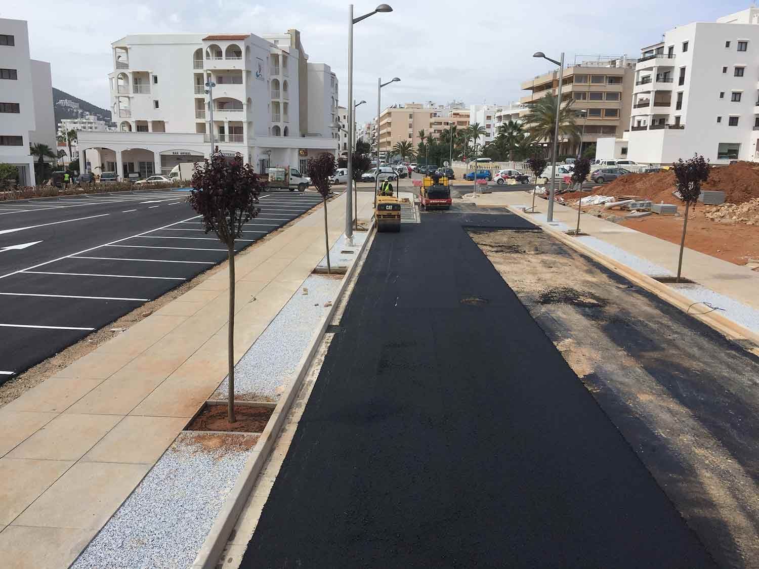 Construcción de carreteras: Trabajadores pavimentan una calle con asfalto negro fresco, bordeada por aceras y edificios.