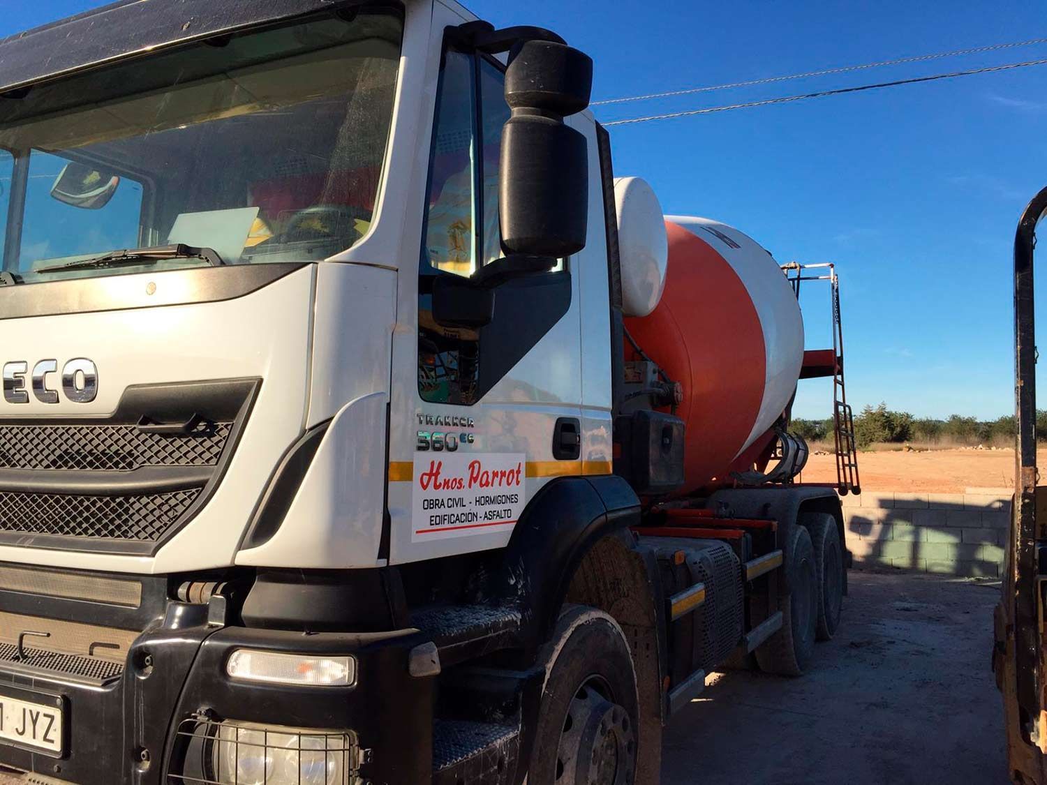 Camión hormigonera estacionado en un día soleado. El camión es blanco, con un bidón rojo y blanco.