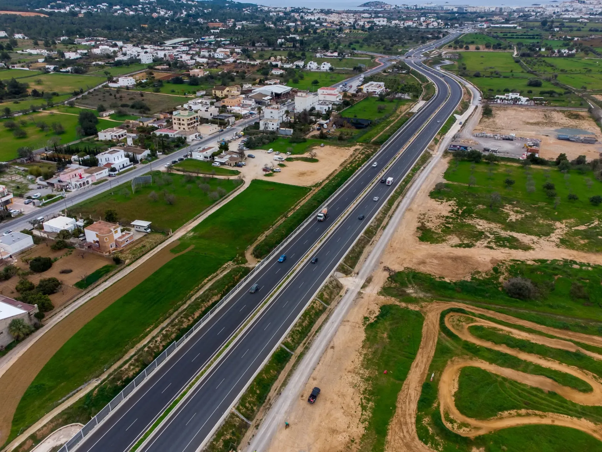 Vista aérea de una carretera de cuatro carriles que atraviesa un paisaje verde cerca de una ciudad costera.