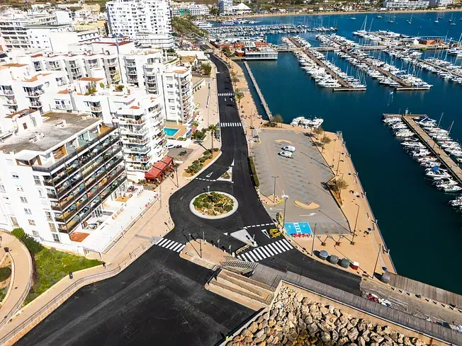 Vista aérea del puerto deportivo con barcos, carretera, rotonda y edificios.