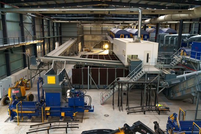 Vista interior de una planta de reciclaje, con maquinaria, cintas transportadoras y una gran empacadora.