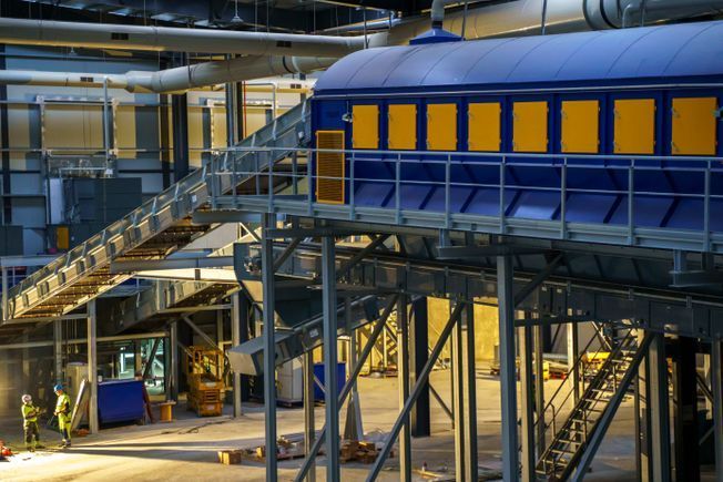 Maquinaria industrial azul y amarilla dentro de un gran edificio. Se ven trabajadores.