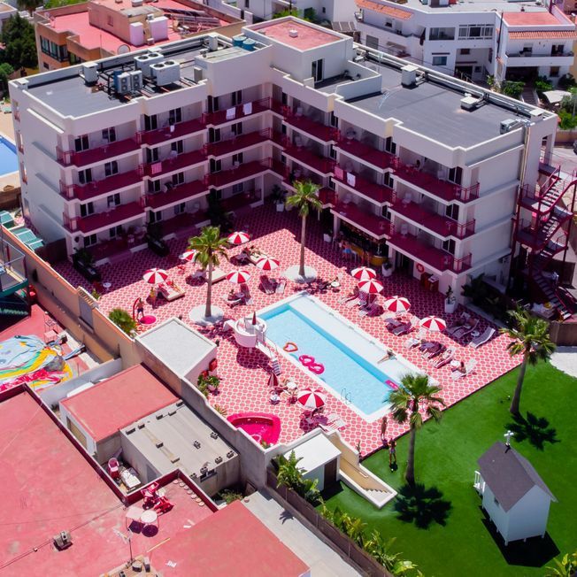 Vista aérea de hotel rosa y blanco con piscina y palmeras.