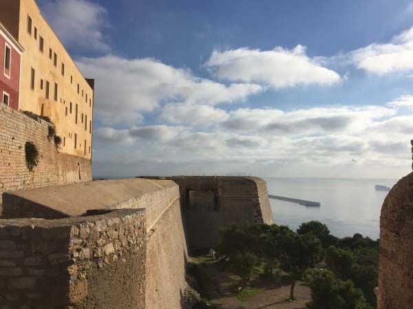 Muros de piedra de una fortaleza con vistas al mar en un día soleado con nubes esponjosas.