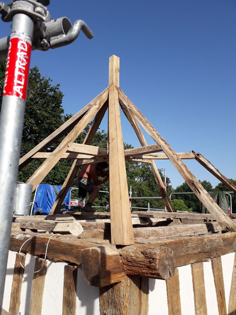 Structure en bois à charpente en A en construction sur un toit, avec un tuyau métallique à gauche.