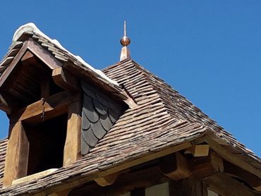 Toit en bois patiné par le temps, recouvert de bardeaux gris et surmonté d'une petite flèche.