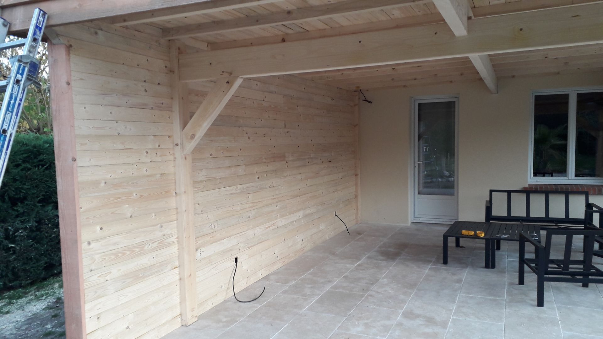 Terrasse couverte en bois avec banc et table intégrés, aménagée sur un sol en pierre.