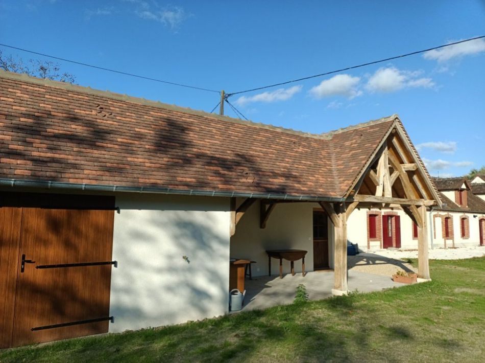 Maison de campagne avec toit de tuiles rouges, murs blancs, portes en bois.