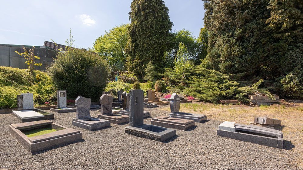 Ein Friedhof voller Gräber und Bäume an einem sonnigen Tag.