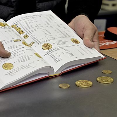 Mains de l'expert tenant un bouquin sur la numismatique