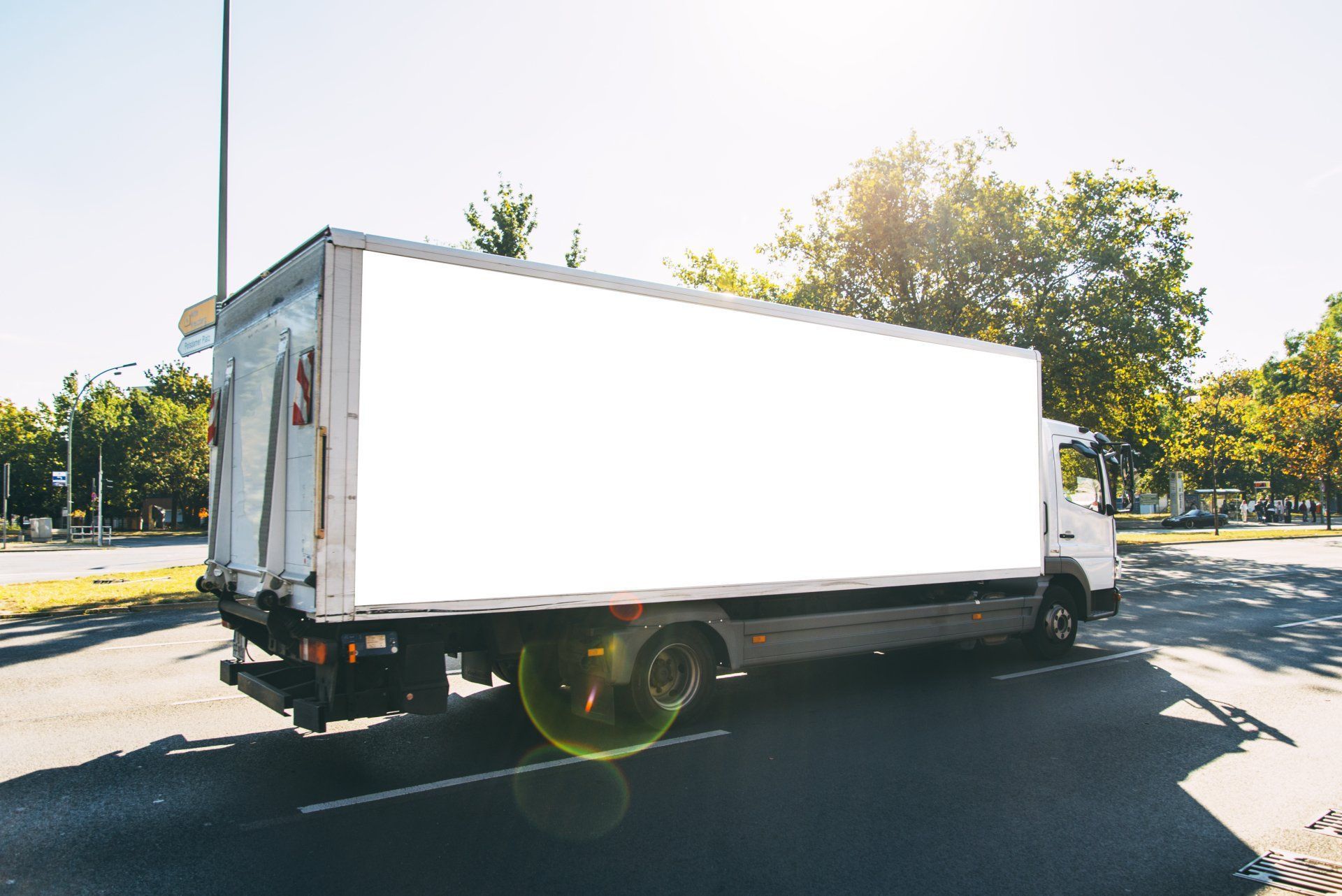 Un camion de livraison blanc est stationné sur une route asphaltée près d'arbres, par une belle journée ensoleillée.