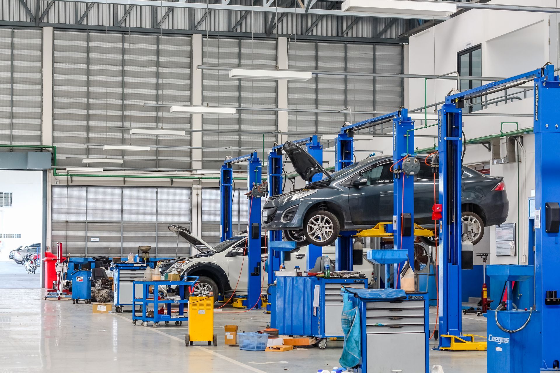 Un atelier de réparation automobile spacieux, avec des voitures surélevées sur des ponts élévateurs bleus et divers outils et équipements posés au sol.