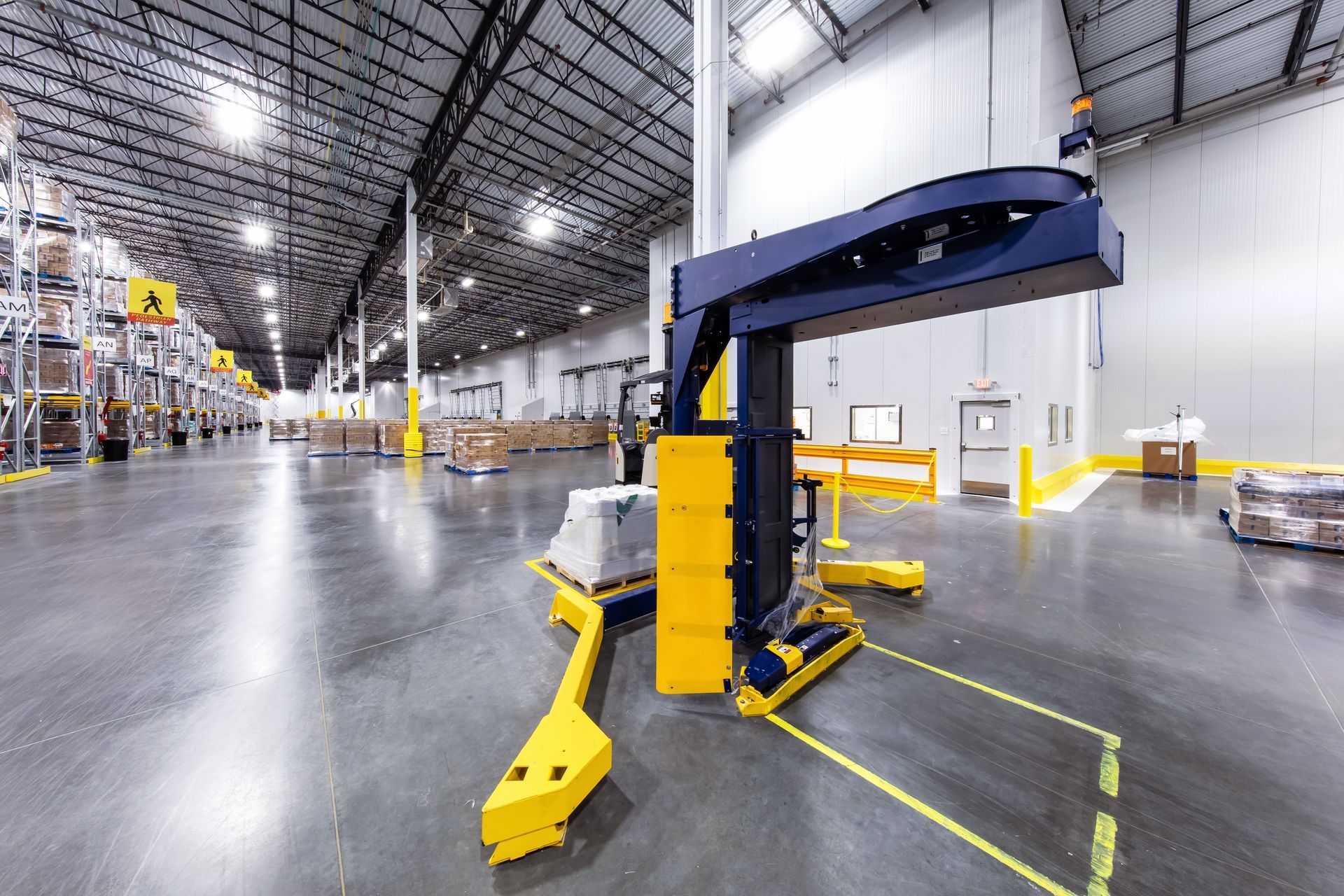 Une machine robotisée industrielle jaune et noire se dresse sur le sol d'un entrepôt, tenant une petite caisse blanche.