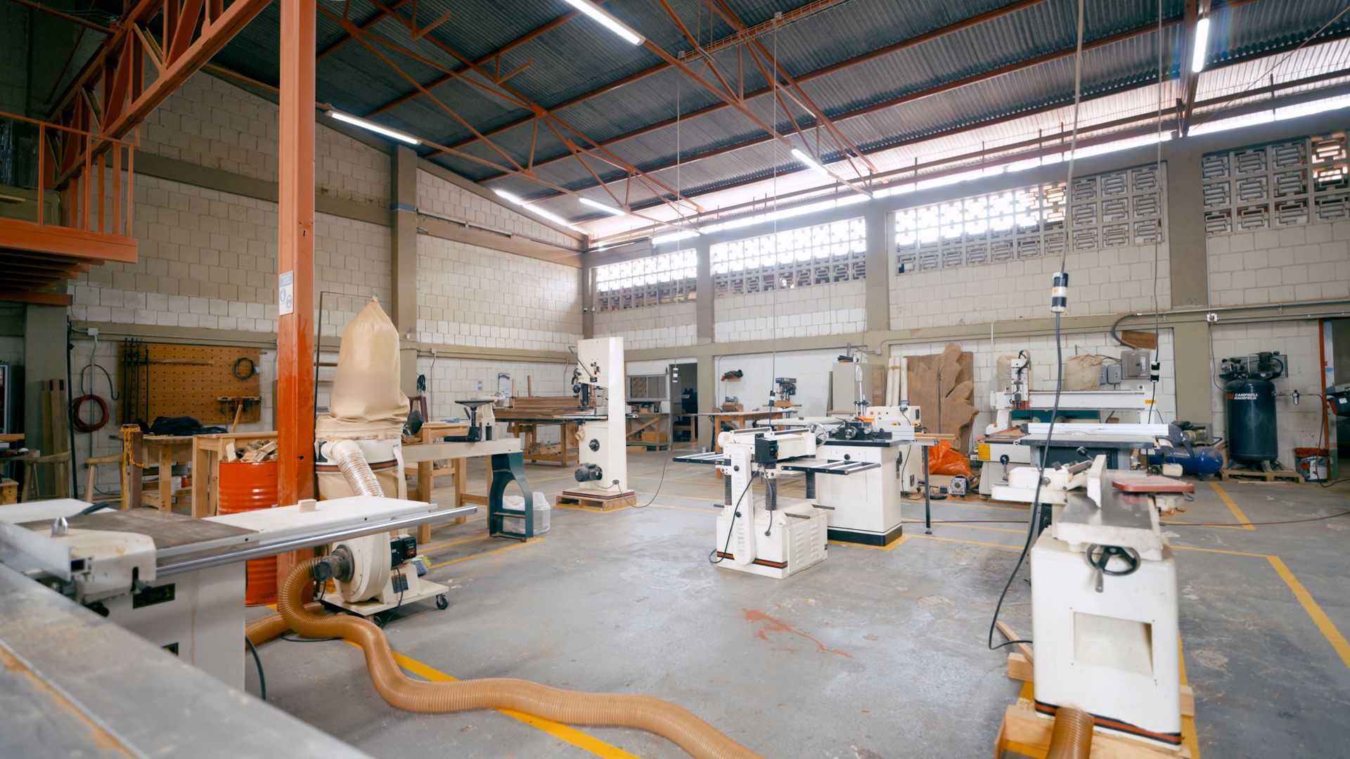 Un atelier de menuiserie spacieux et bien éclairé, équipé de machines industrielles, de postes de travail et d'un sol en béton.