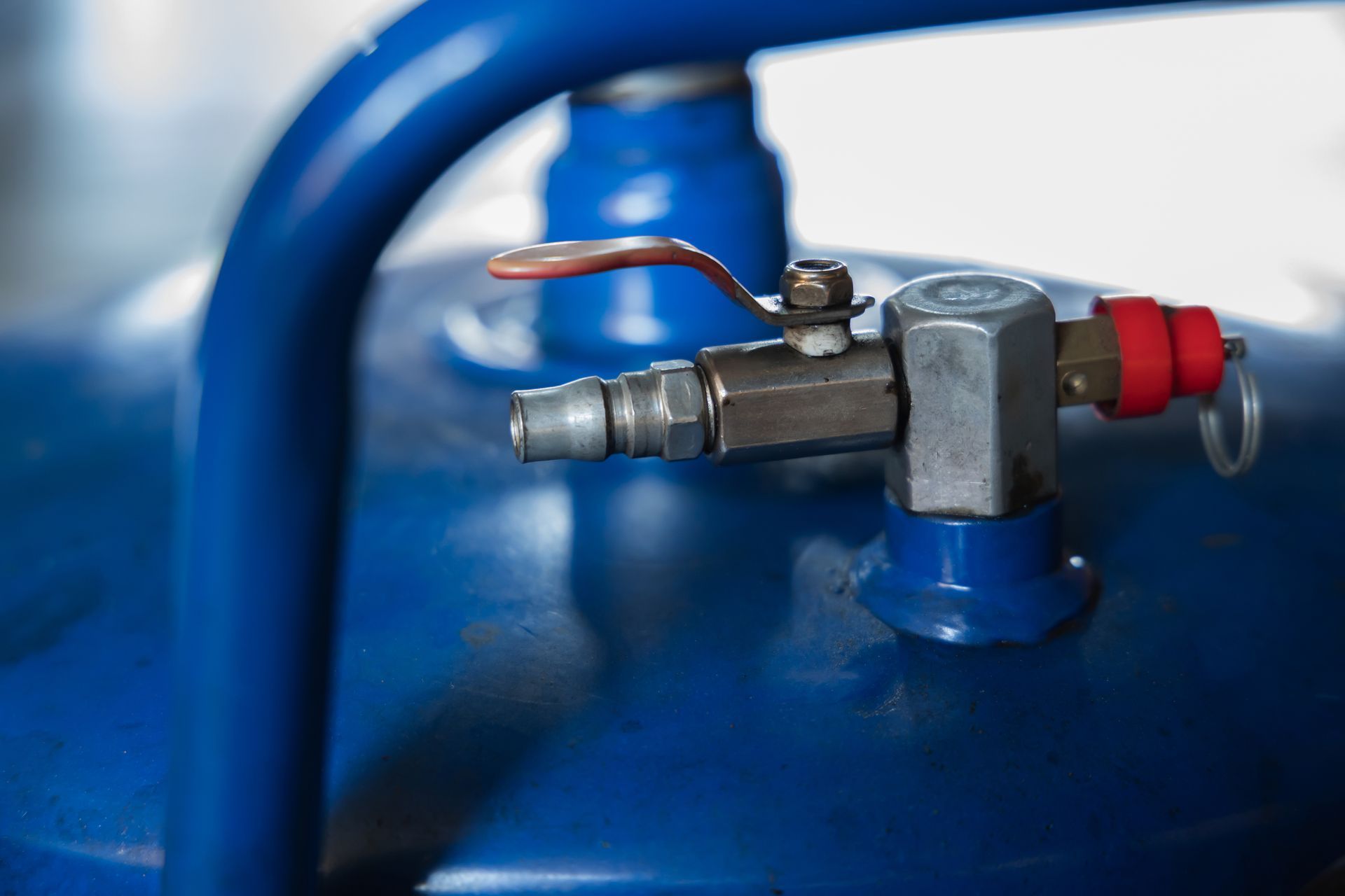 Gros plan sur un réservoir bleu de compresseur d'air comportant une valve métallique, un raccord de tuyau d'air et un petit bouchon de sécurité rouge.