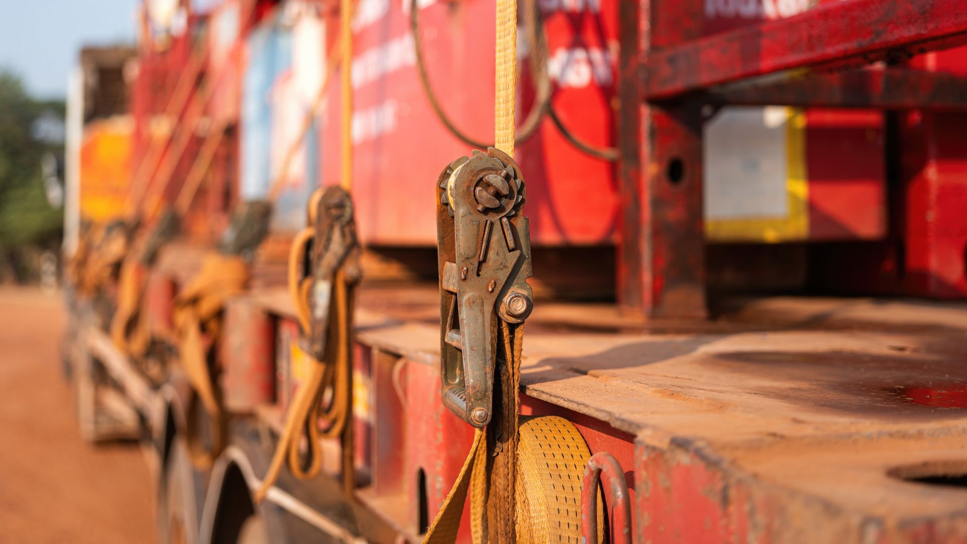 Gros plan sur une boucle de sangle à cliquet métallique sur une remorque de camion plateau rouge.