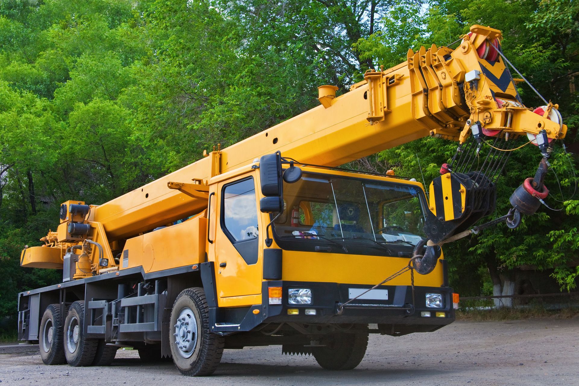 Une grue de chantier mobile jaune vif est stationnée sur une surface de gravier devant une végétation luxuriante.