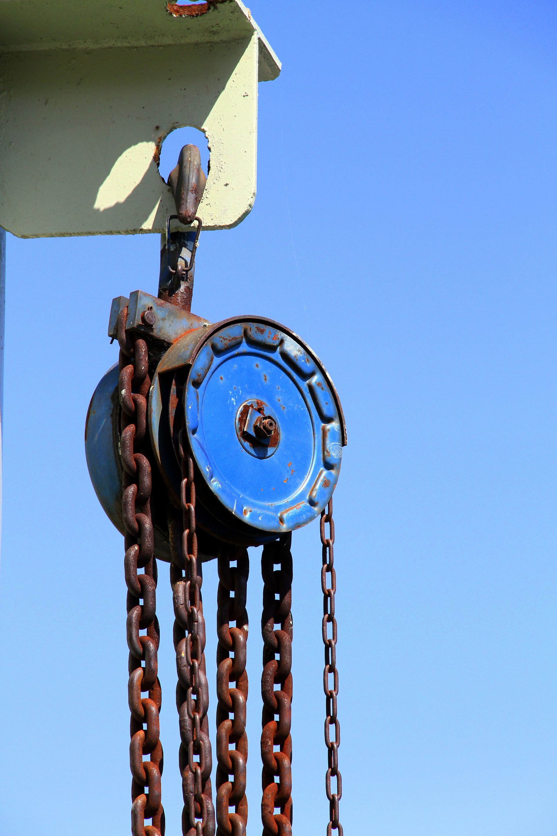 Un palan à chaîne bleue est suspendu à une poutre métallique sur fond de ciel bleu clair.