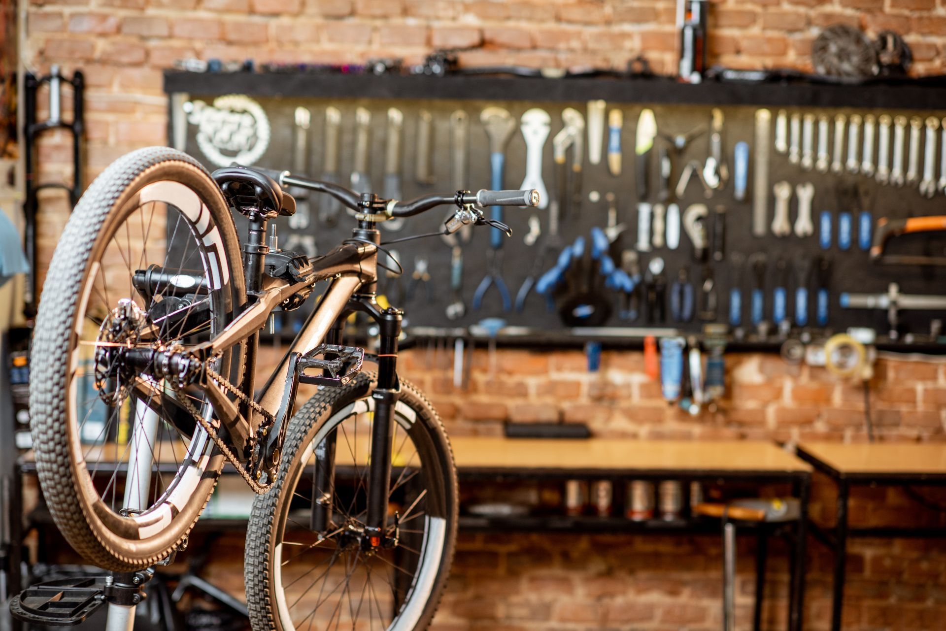 Un VTT suspendu à un support de réparation, placé devant un mur où sont rangés des outils dans un atelier.