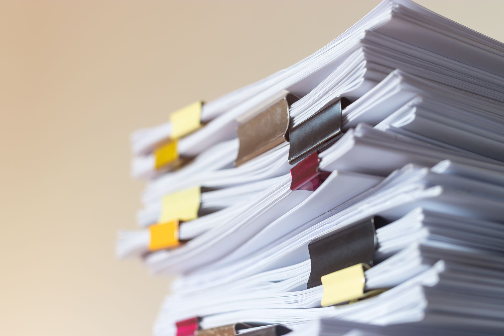 Une pile de documents en papier blanc, maintenus par des pinces à reliure métalliques de différentes couleurs.