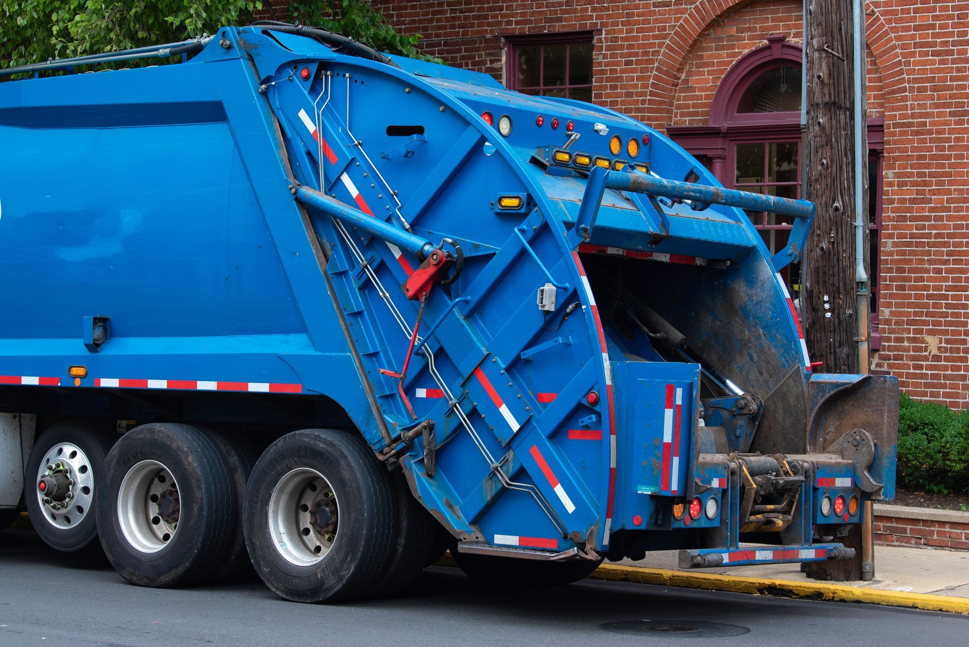 Un camion-poubelle industriel bleu vif est stationné dans une rue à côté d'un bâtiment en briques.