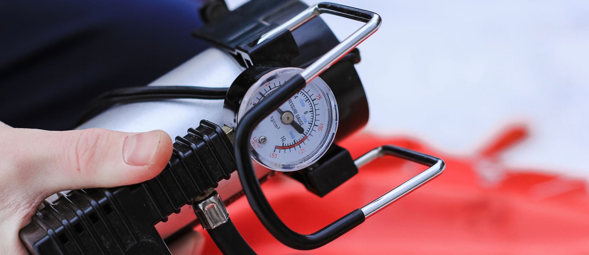 Gros plan sur une personne tenant un gonfleur de pneus portable noir avec un manomètre analogique.