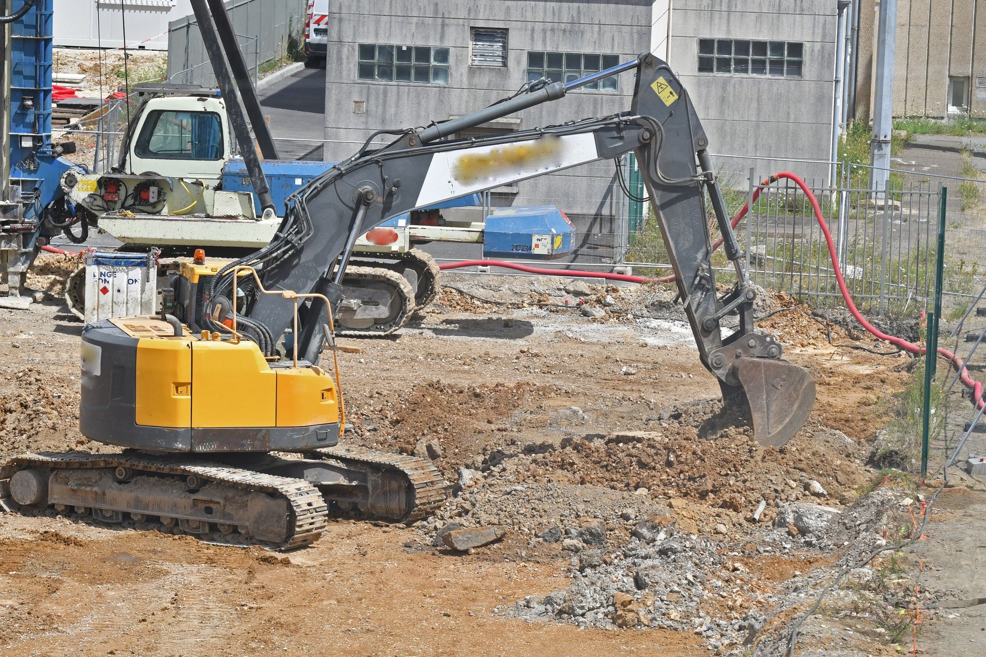 Une excavatrice jaune et grise est posée sur un chantier de construction en terre, son godet positionné près du sol.