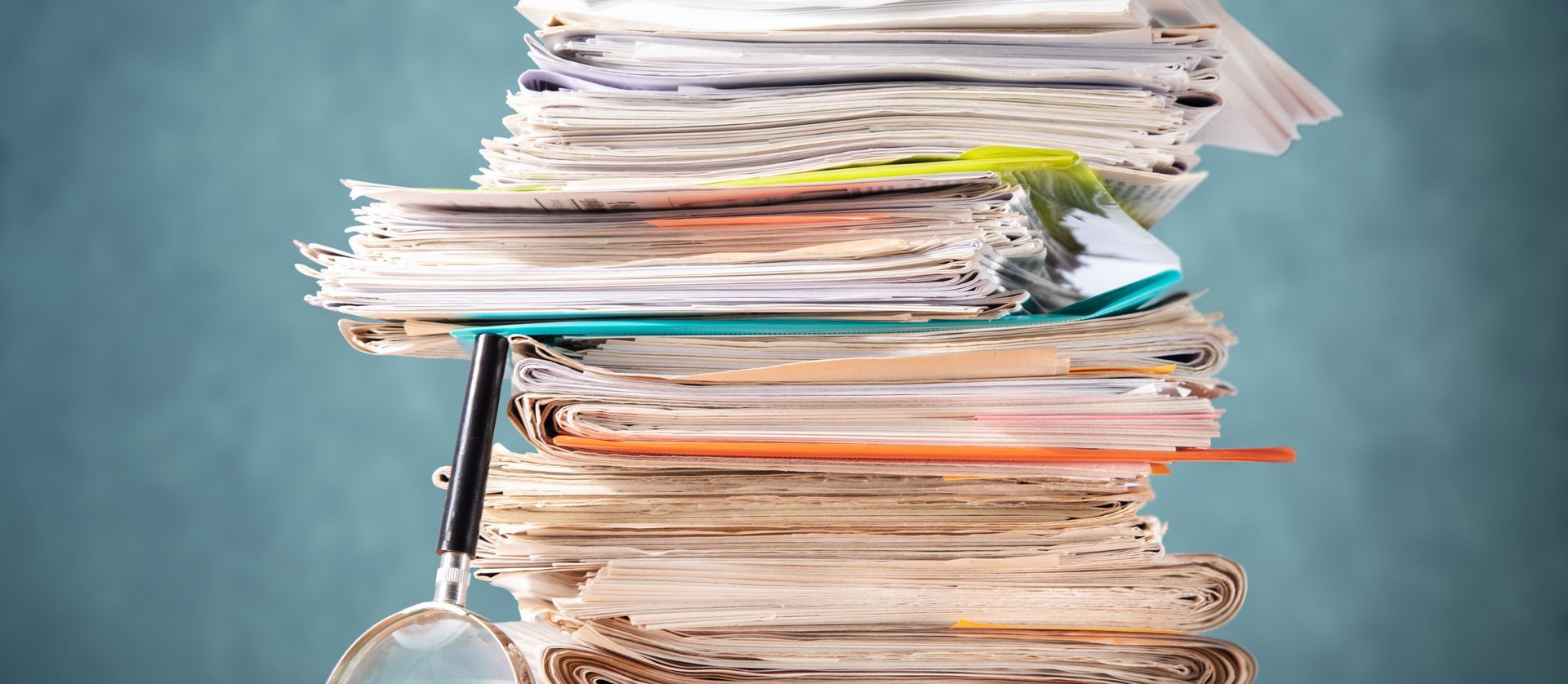 Une grande pile de papiers en désordre, avec une loupe appuyée contre elle.