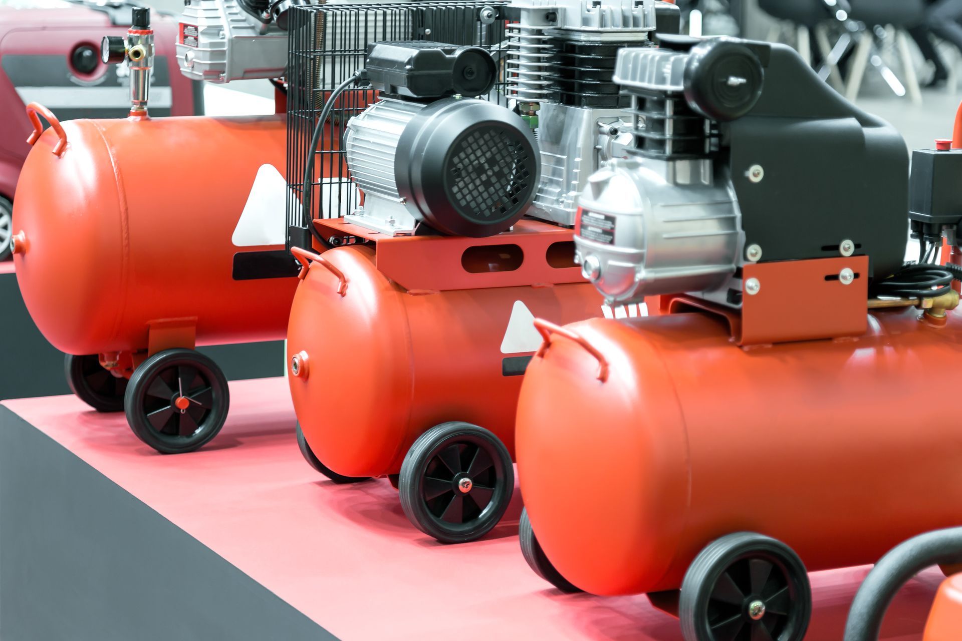 Une rangée de compresseurs d'air orange vif, avec des moteurs et des roues noirs, disposés sur un sol rougeâtre.
