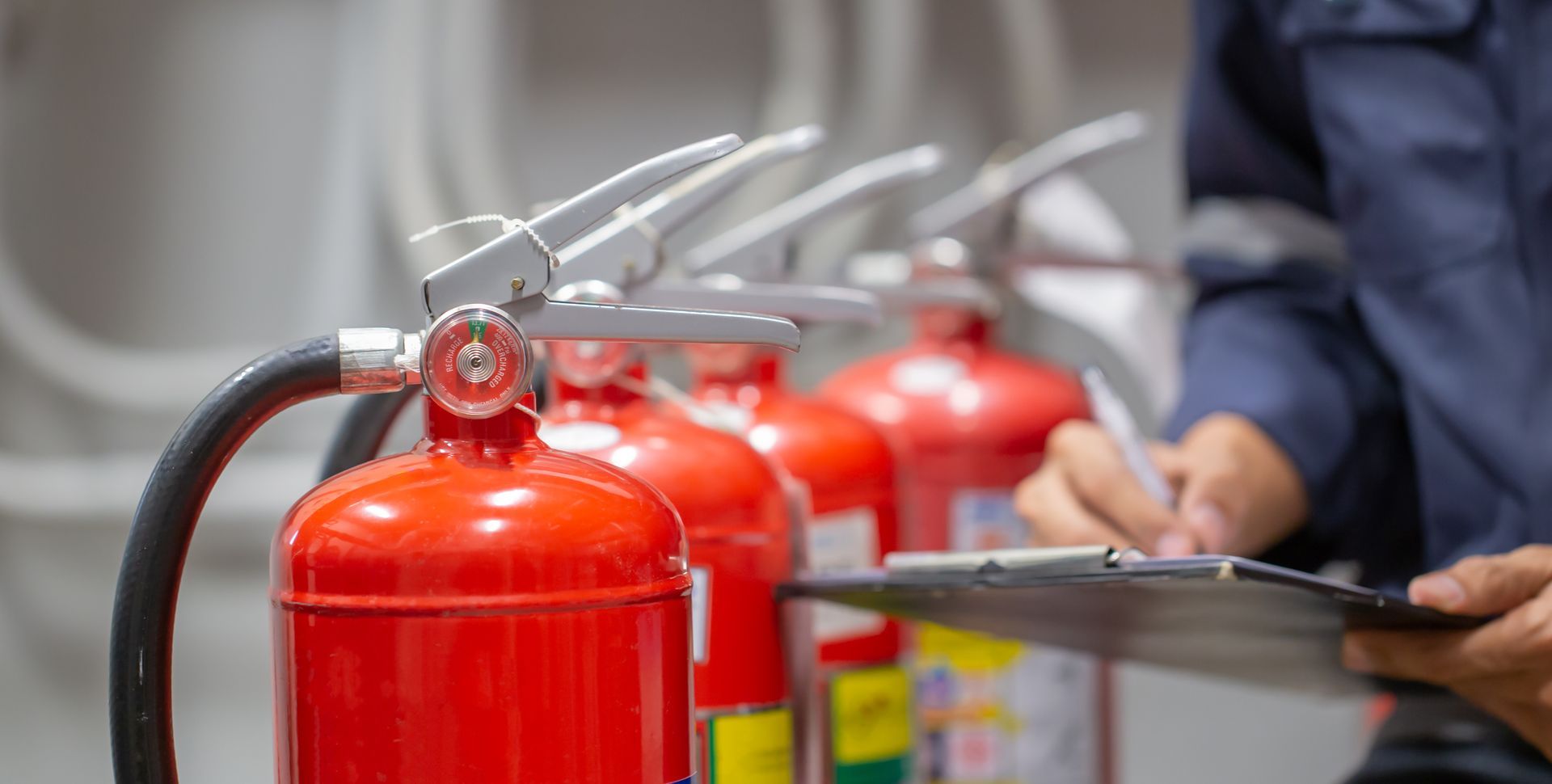 Un employé en uniforme bleu vérifie une rangée d'extincteurs rouges tout en tenant un bloc-notes.