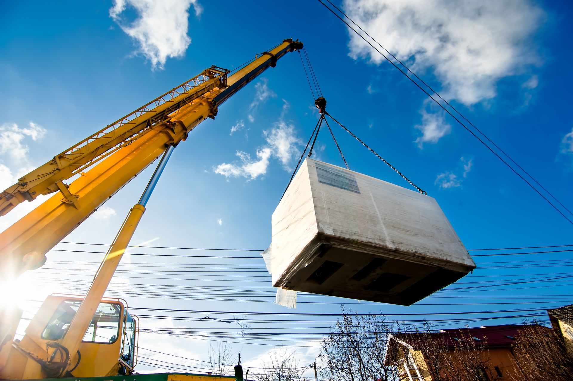 Une grue de chantier jaune soulève un gros bloc de béton blanc sur fond de ciel bleu éclatant.