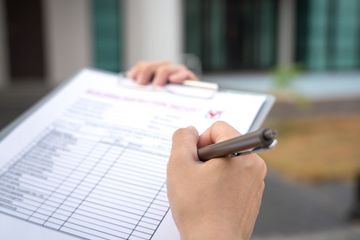 Gros plan sur une personne remplissant un formulaire sur un bloc-notes tenu à l'extérieur.