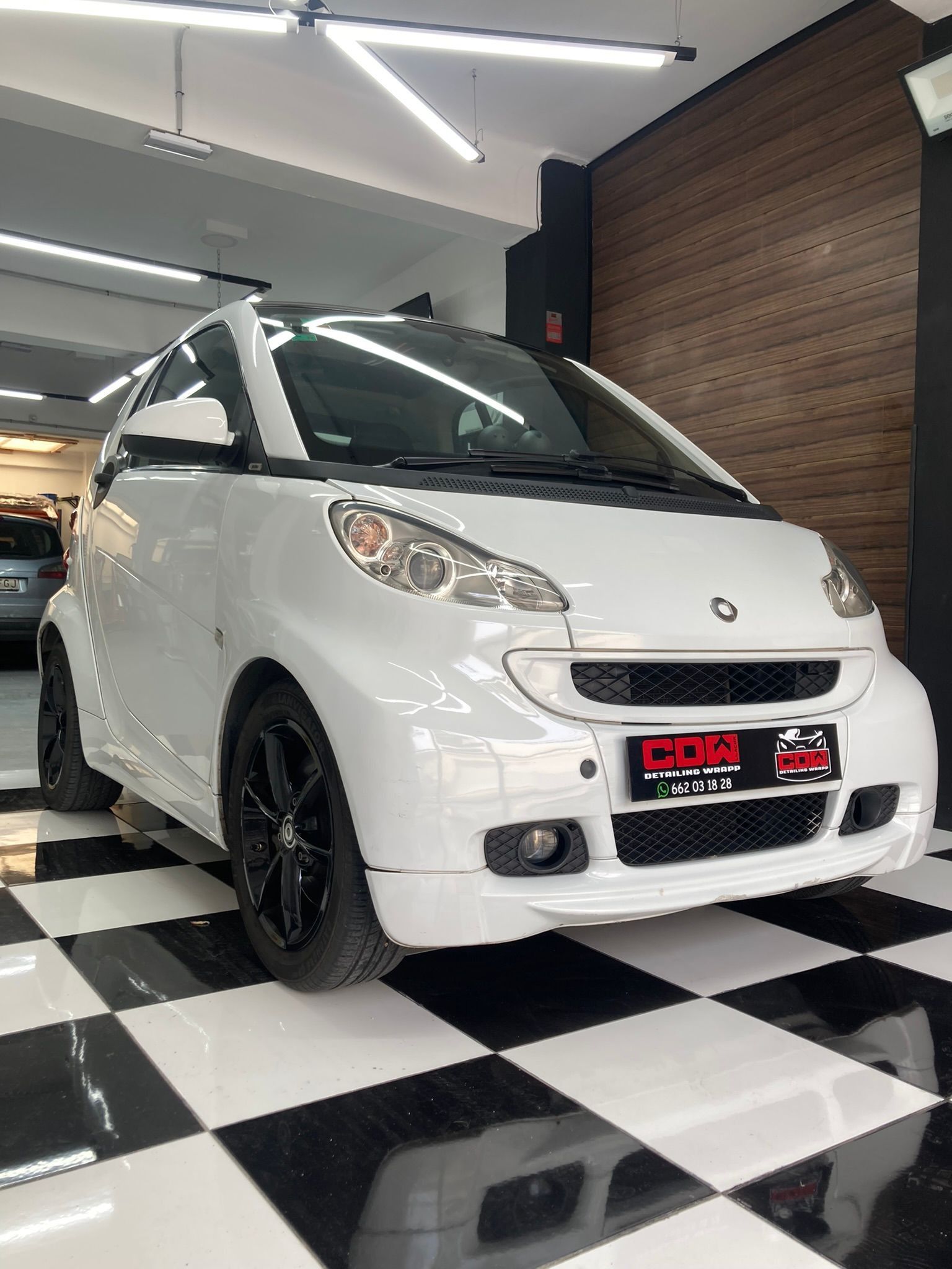 Un coche inteligente de color blanco está aparcado en un garaje sobre un suelo cuadriculado.