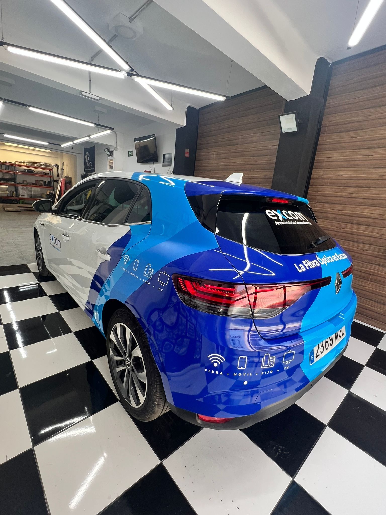 Un coche azul y blanco está aparcado sobre un suelo a cuadros en un garaje.